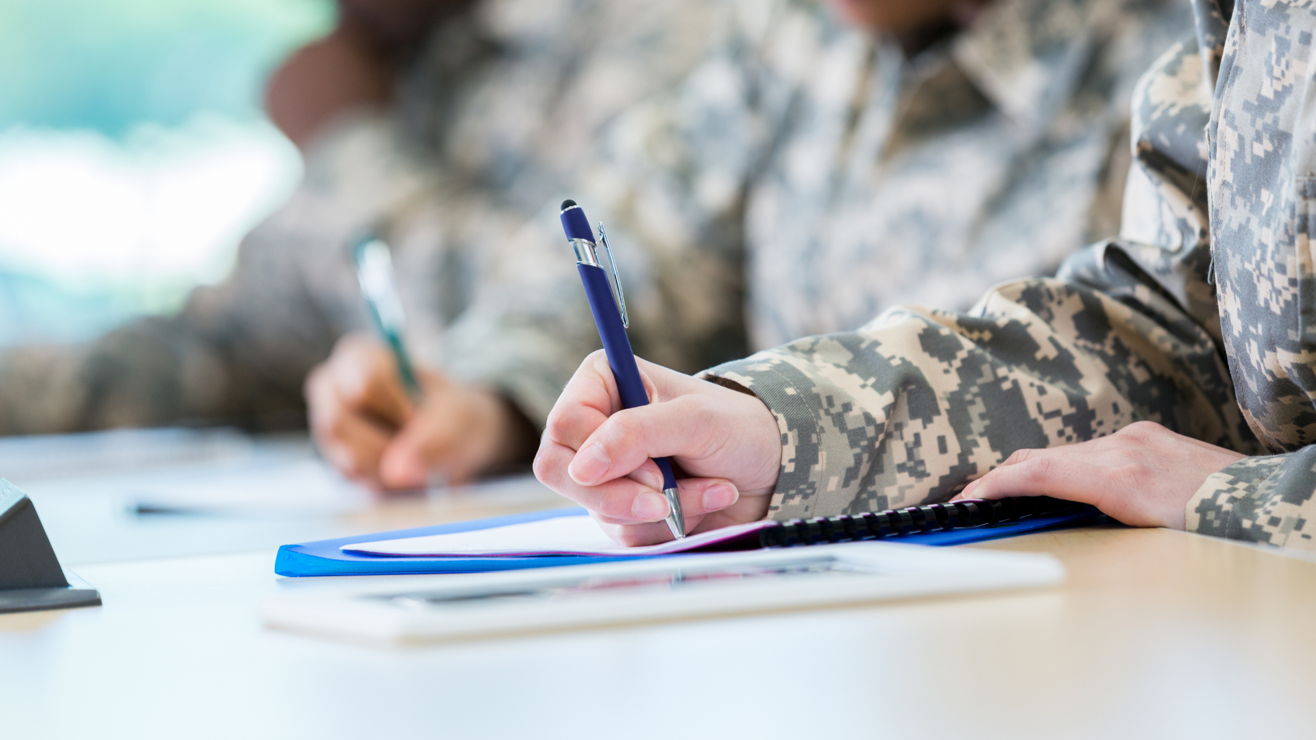 Soldiers writing on clipboards, detail shot of hands and camouflage uniforms.