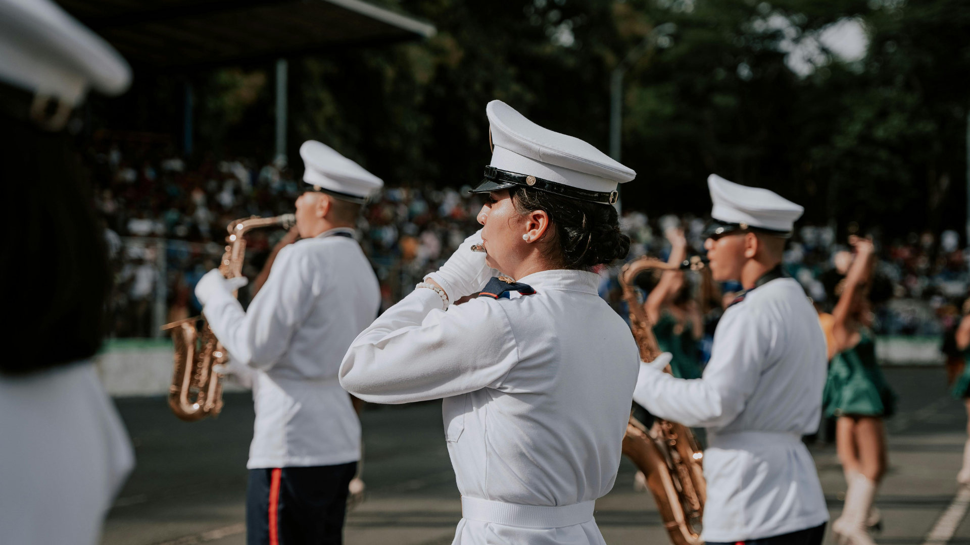 Marching band members in white uniforms playing instruments outdoors.