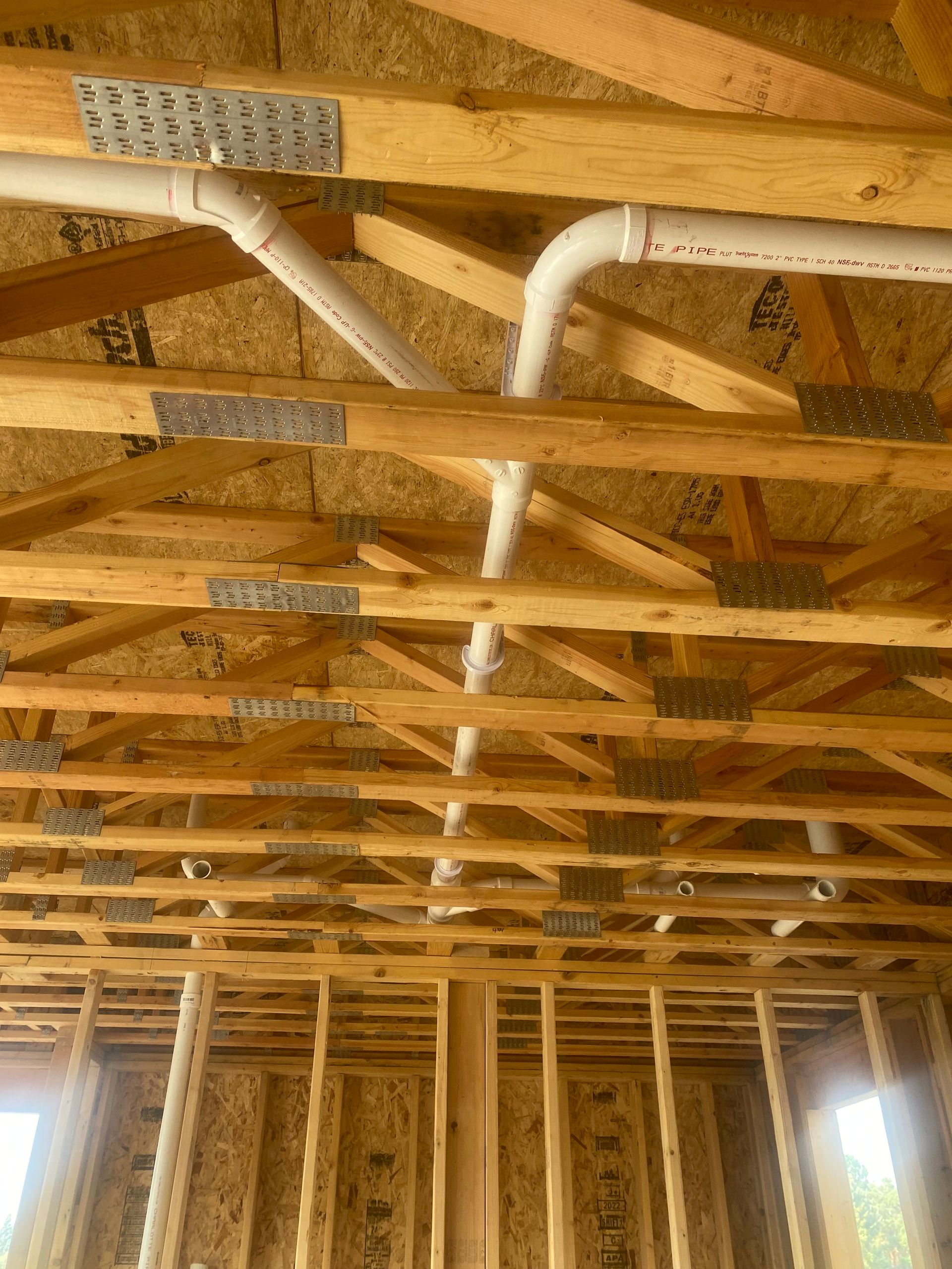 The ceiling of a house under construction with wooden beams and pipes.