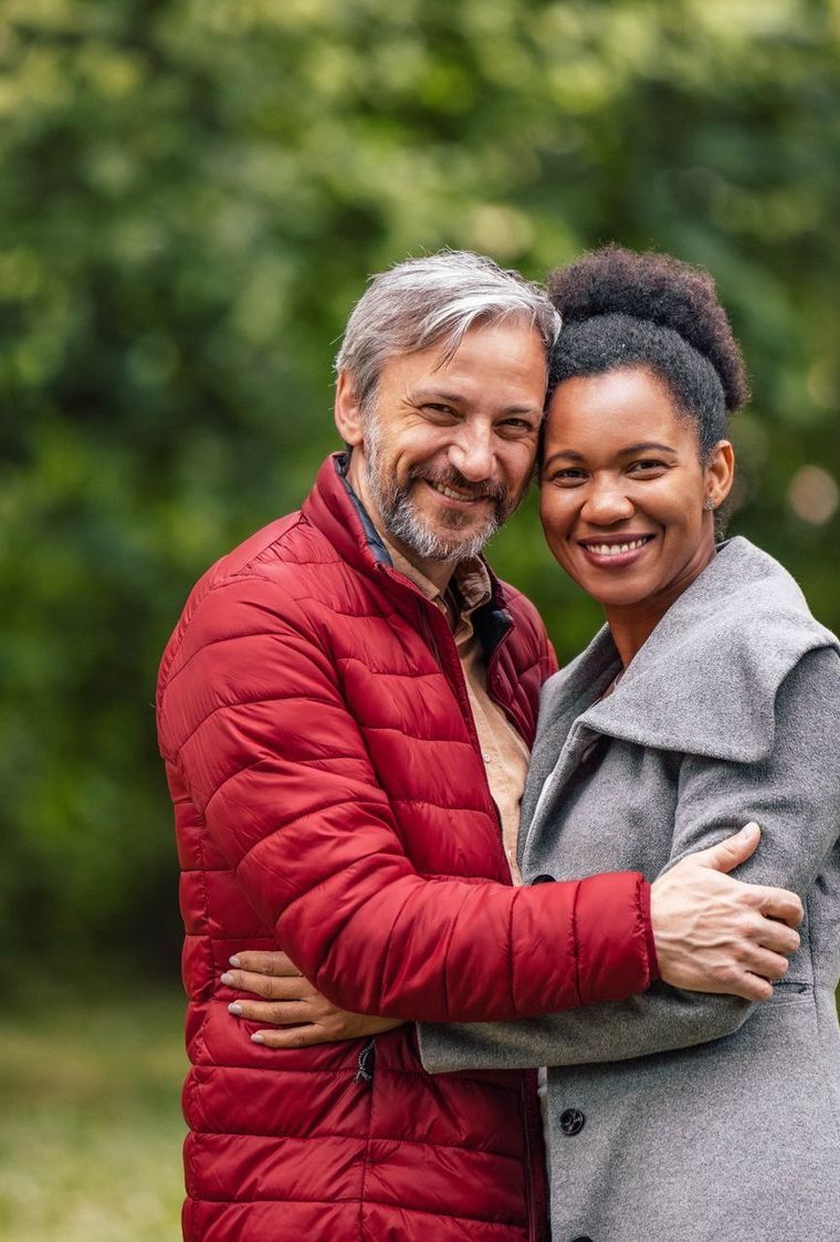A man and a woman are hugging each other in a park.