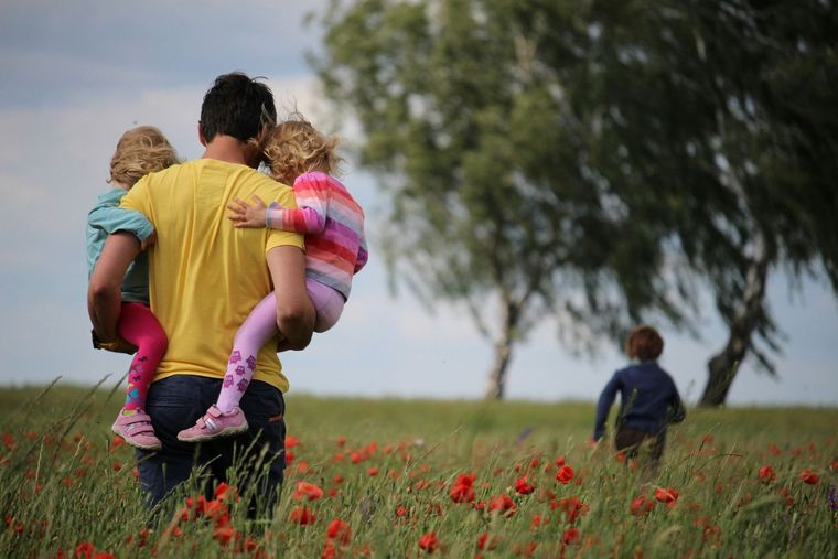 A man is holding two children in a field of flowers.
