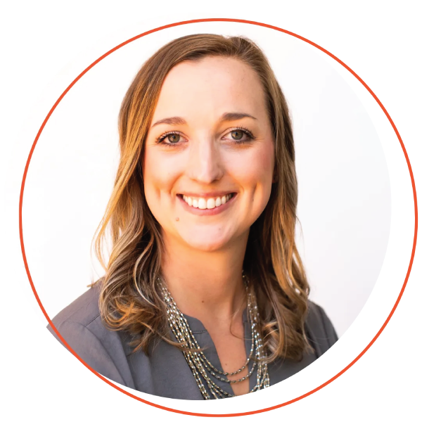 Smiling woman with short blonde hair, wearing a blue-green shirt and layered necklace, outdoors.