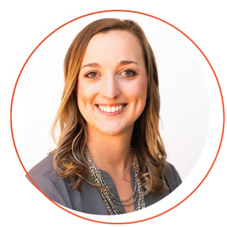 Smiling woman with short blonde hair, wearing a blue-green shirt and layered necklace, outdoors.