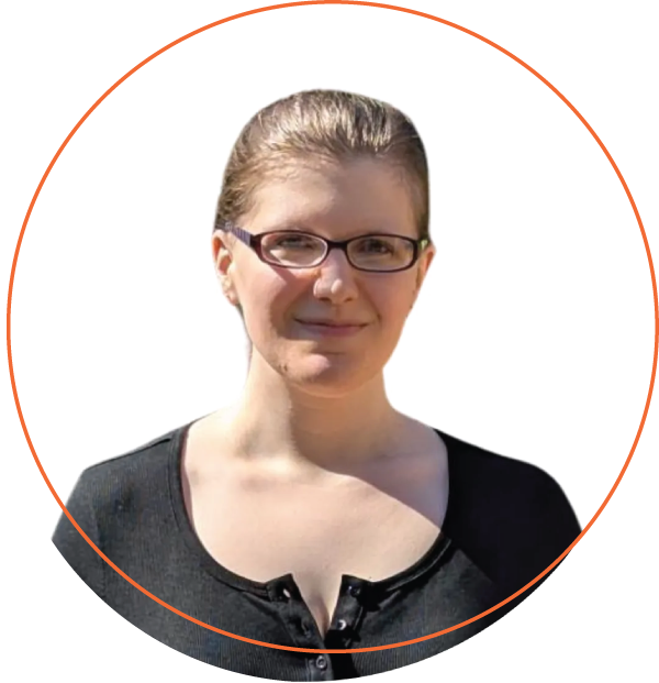 Smiling woman with short blonde hair, wearing a blue-green shirt and layered necklace, outdoors.