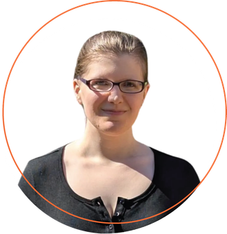 Smiling woman with short blonde hair, wearing a blue-green shirt and layered necklace, outdoors.