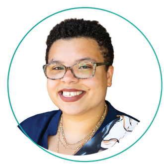 Smiling woman with glasses and short curly hair, wearing a blue top against a white background.