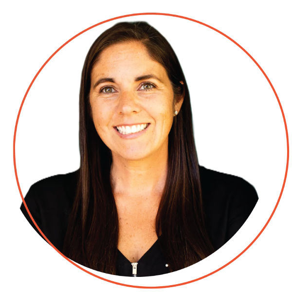 Smiling woman with short blonde hair, wearing a blue-green shirt and layered necklace, outdoors.