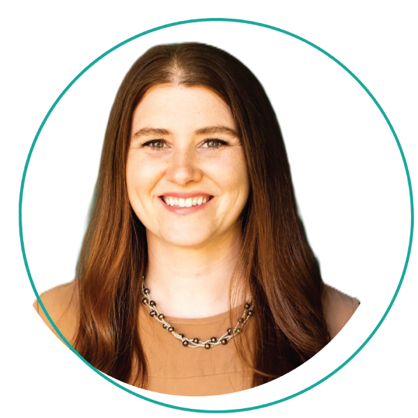 Smiling woman with short blonde hair, wearing a blue-green shirt and layered necklace, outdoors.