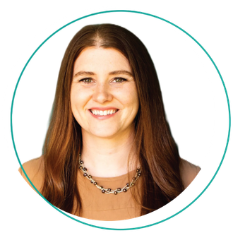 Smiling woman with short blonde hair, wearing a blue-green shirt and layered necklace, outdoors.