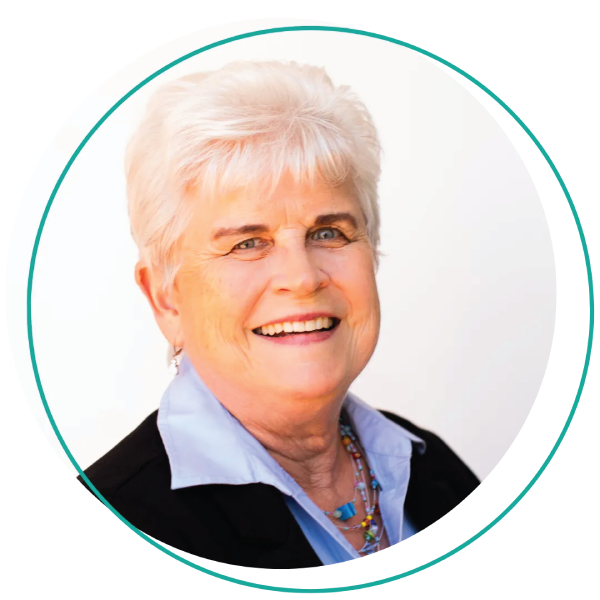 Smiling woman with short blonde hair, wearing a blue-green shirt and layered necklace, outdoors.