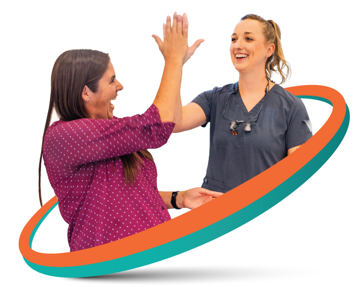 Woman high-fives dental professional holding a clipboard. They are inside a dental office, smiling.