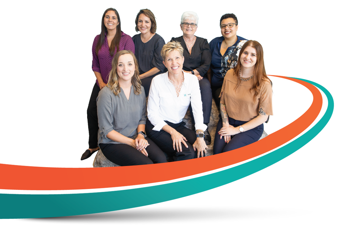 Three people, a man in a lab coat holding a clipboard, and two women, smiling, stand near a curved orange and teal line.