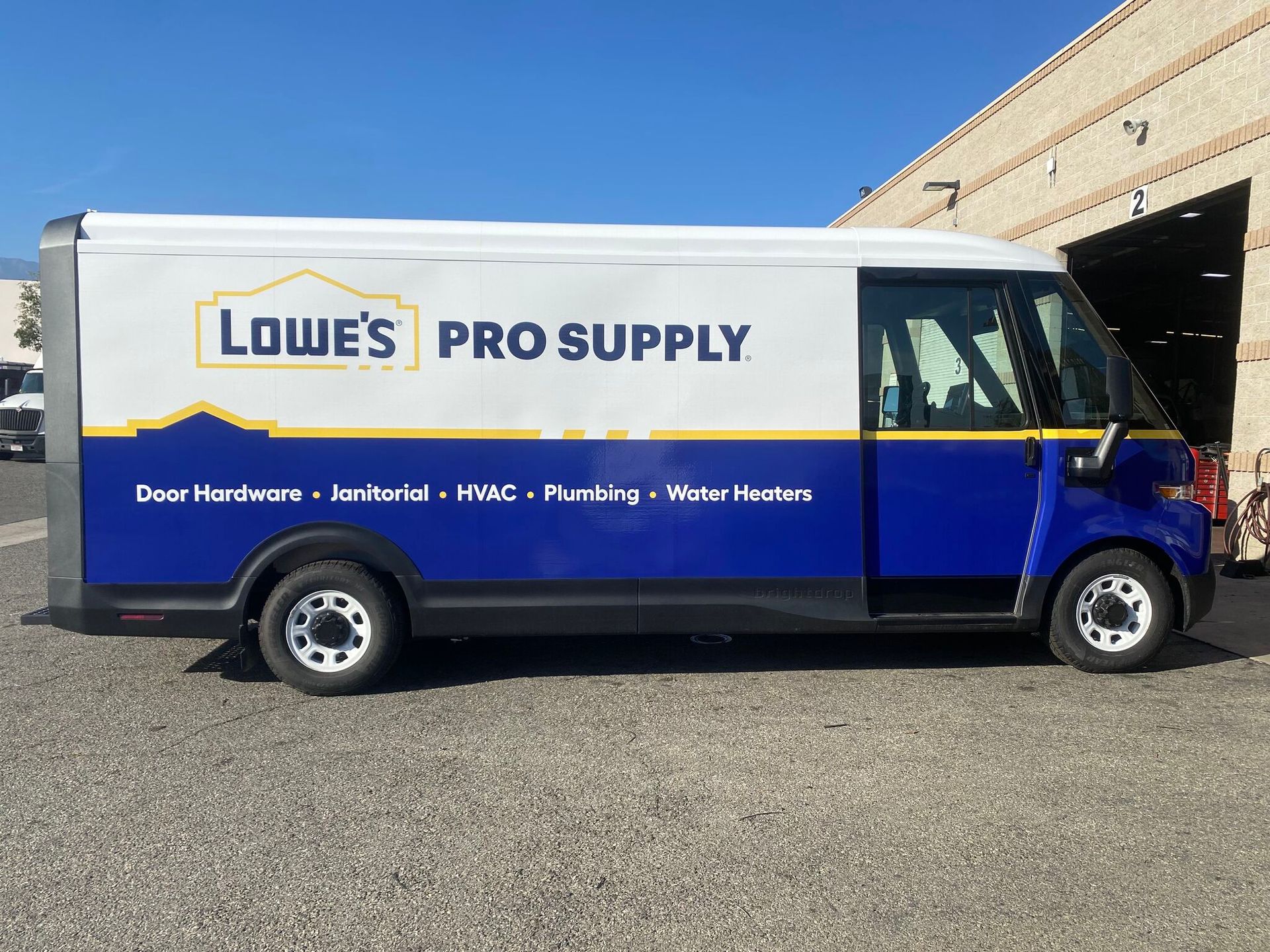 A Lowe’s Pro Supply delivery van parked on a gravel lot next to a brick building.