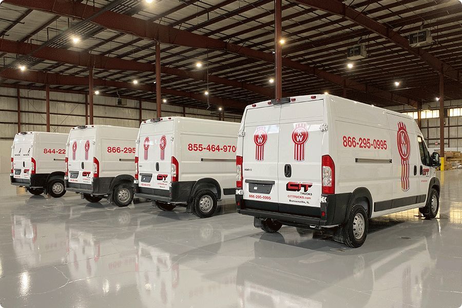 Four white service vans with red logos parked inside a large warehouse.