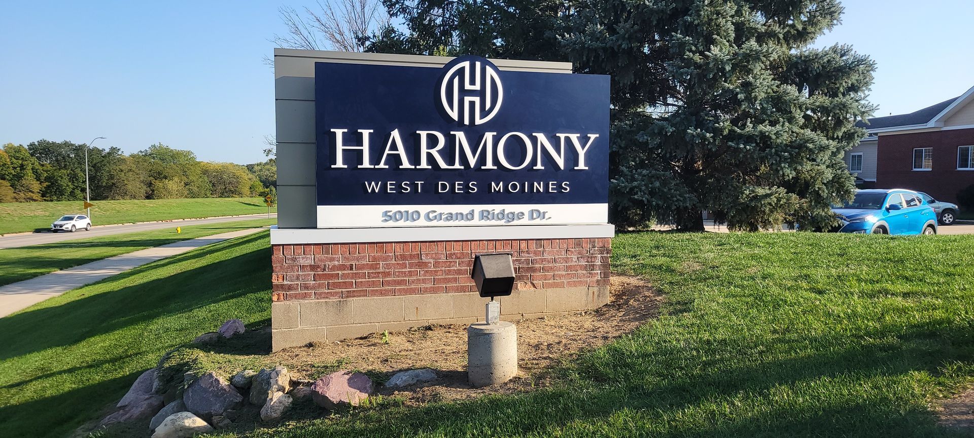 Sign for Harmony West Des Moines, a teal and white sign with brick at the base.
