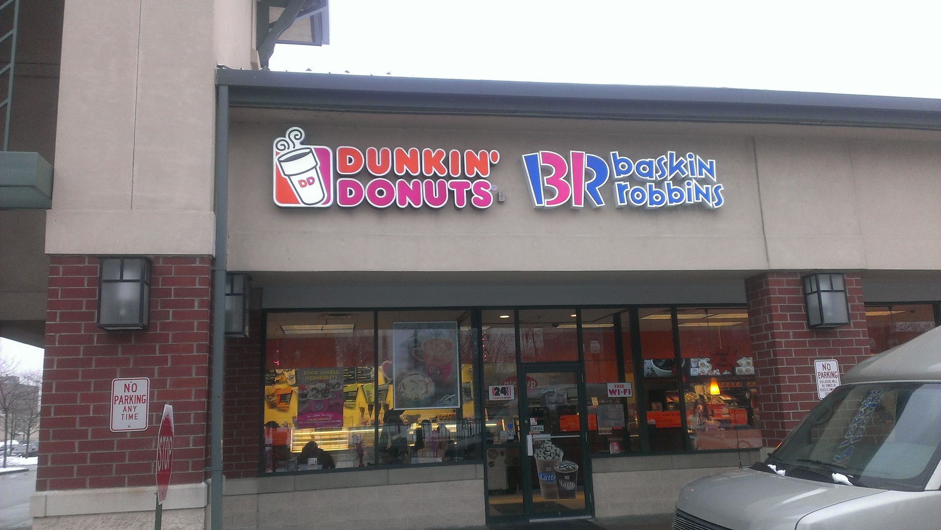 Dunkin' Donuts and Baskin-Robbins storefront with sign, windows, and brick facade. Gray van parked in front.