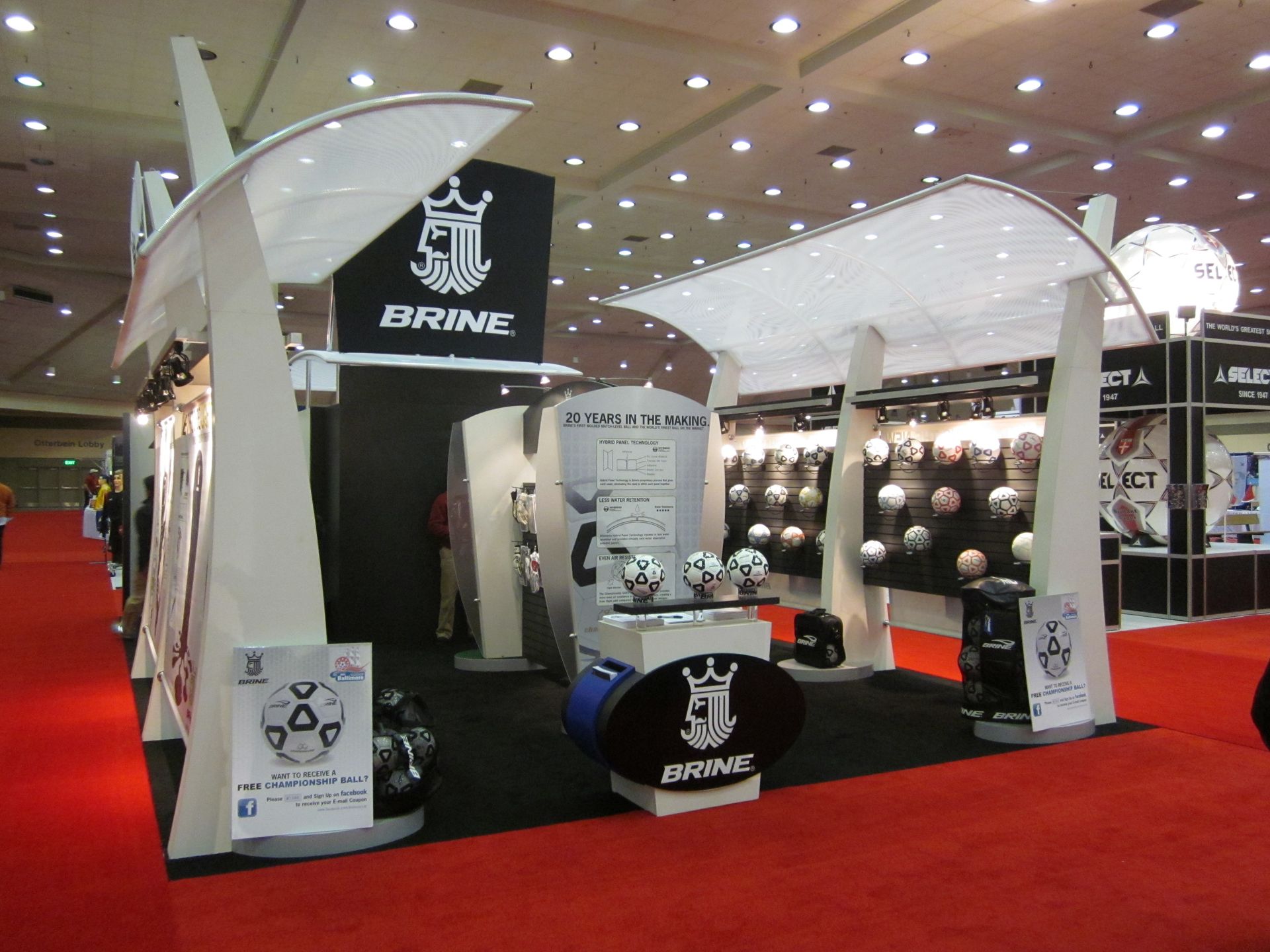 Brine soccer booth at a trade show. White canopy over display of soccer balls and gear on red carpet.