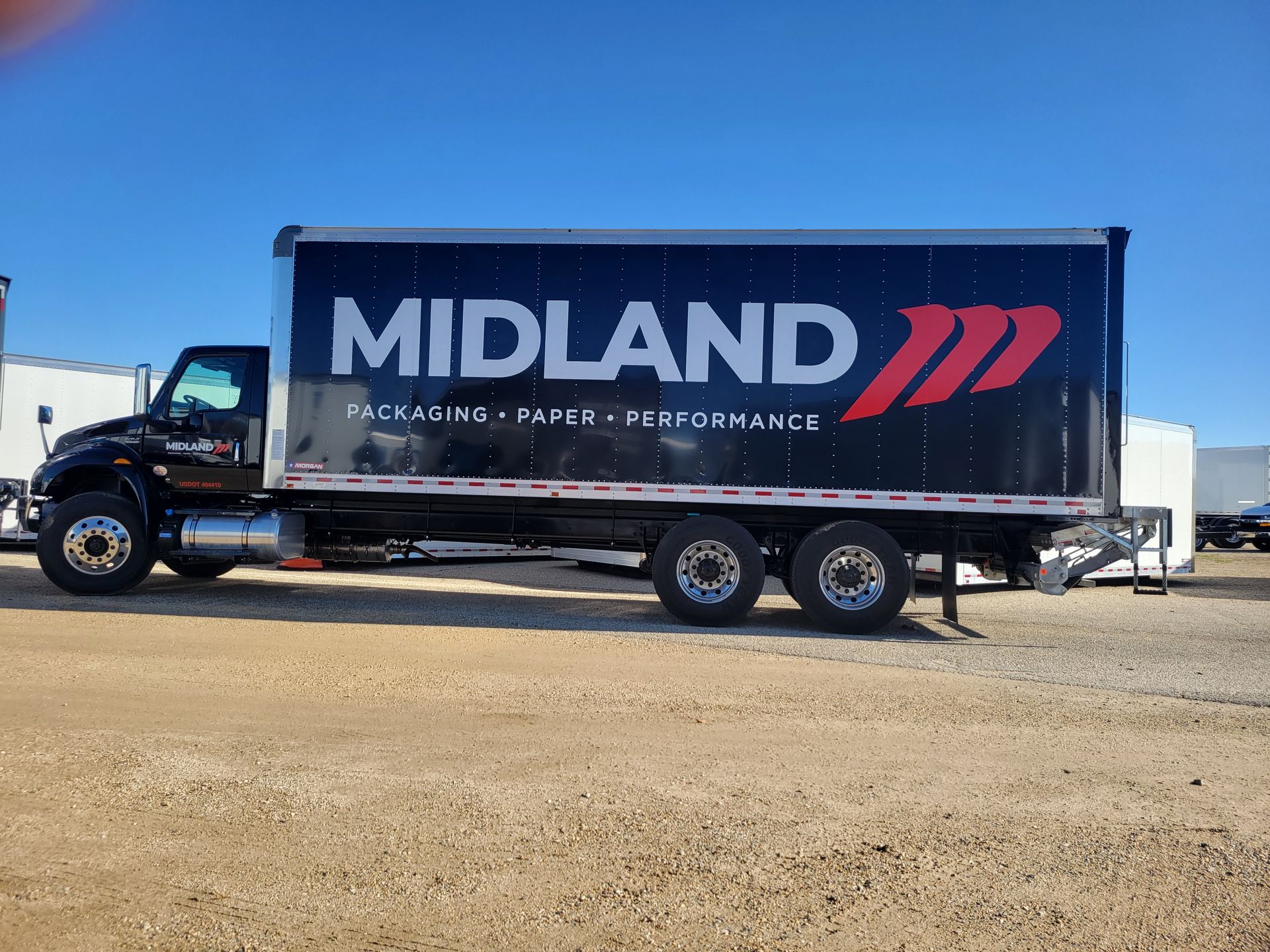 Black Midland truck with white text and red arrow, parked on gravel against blue sky.