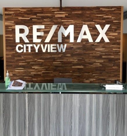 RE/MAX Cityview sign on a wood-paneled wall, above a gray and glass reception desk.