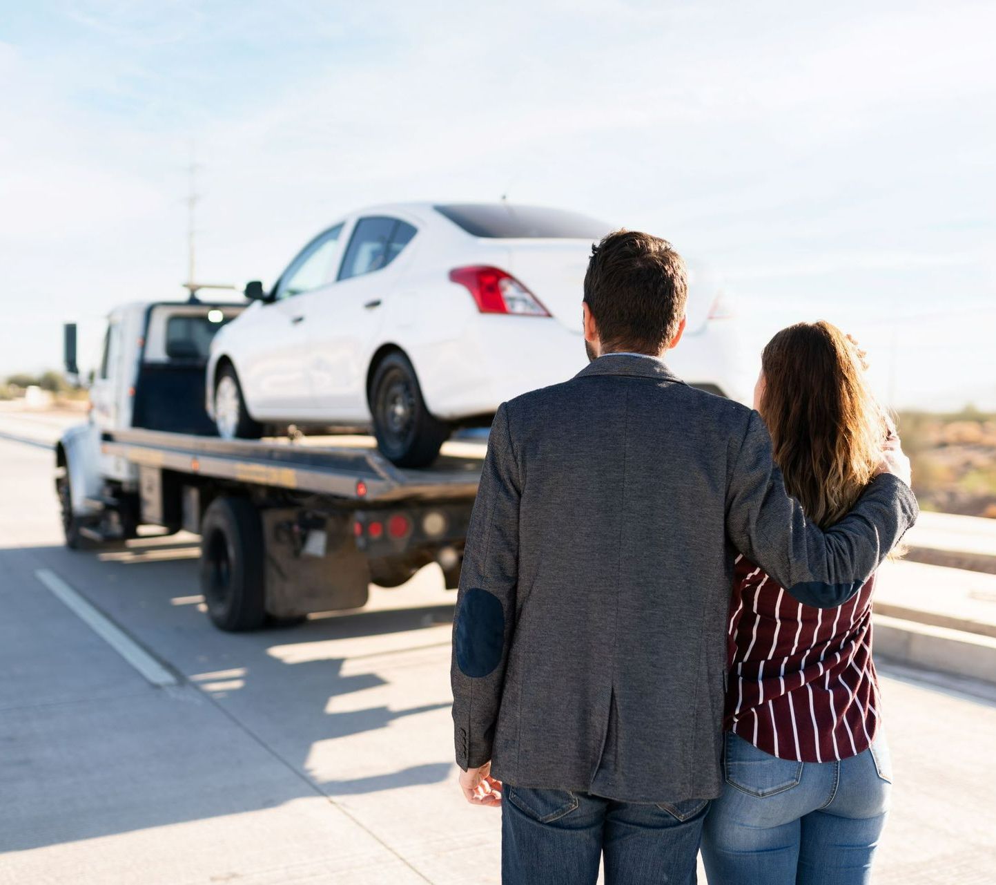 A man and woman are standing next to a tow truck with a car on the back.