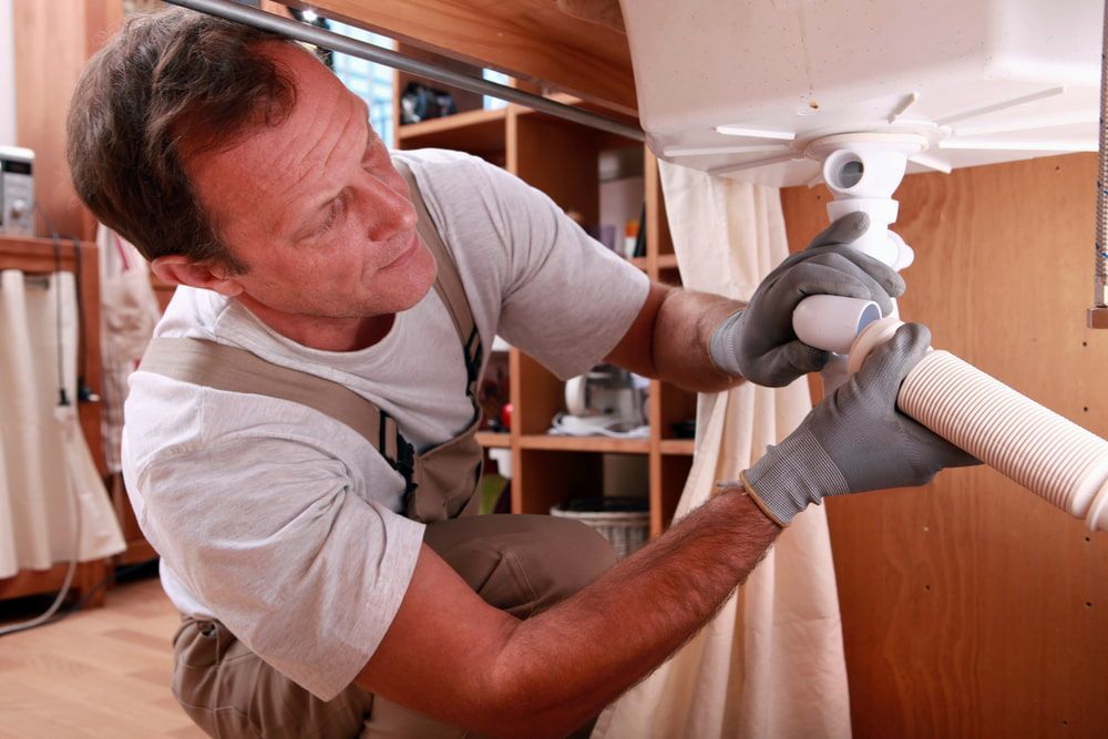 A Man Is Fixing A Sink Pipe In A Kitchen — Ashley Chick Plumbing In Baranduda, VIC