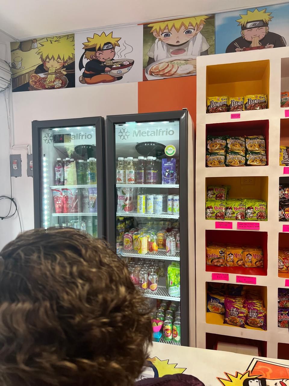 Una persona está parada frente a un refrigerador lleno de bebidas.