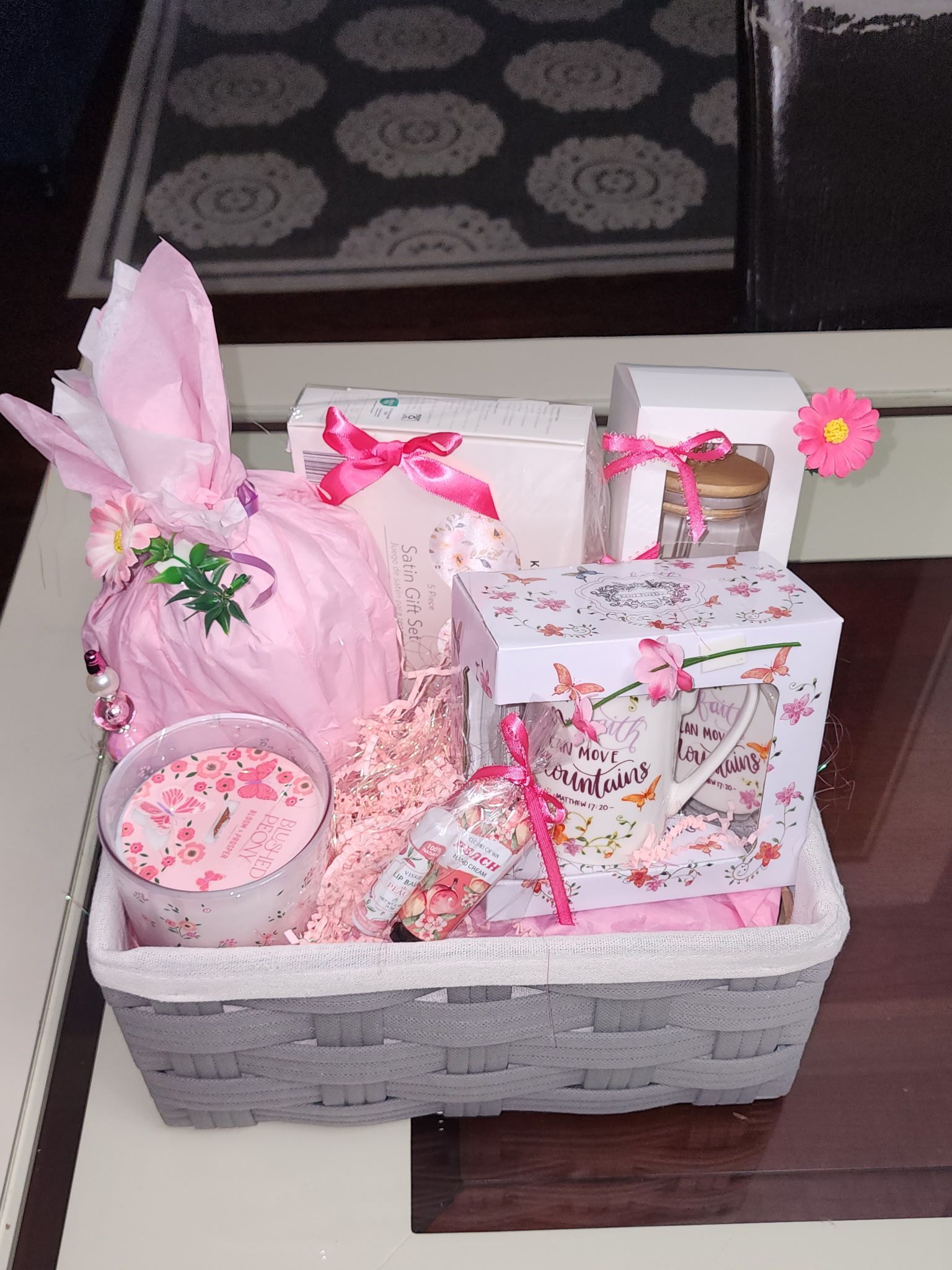 Gift basket with pink and white items: candle, wrapped gifts, and a mug.