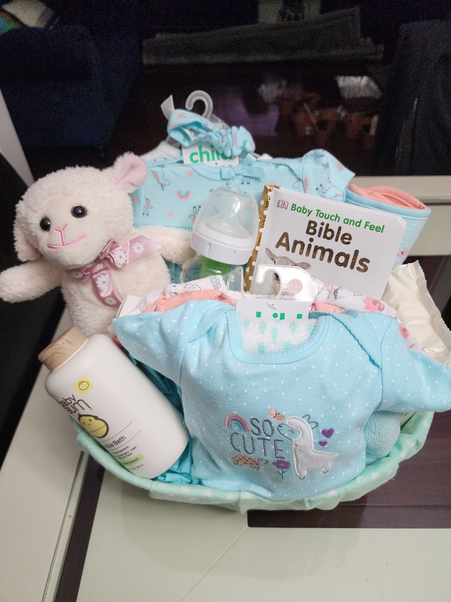 Baby gift basket with clothing, lamb plush, bottle, and a book.