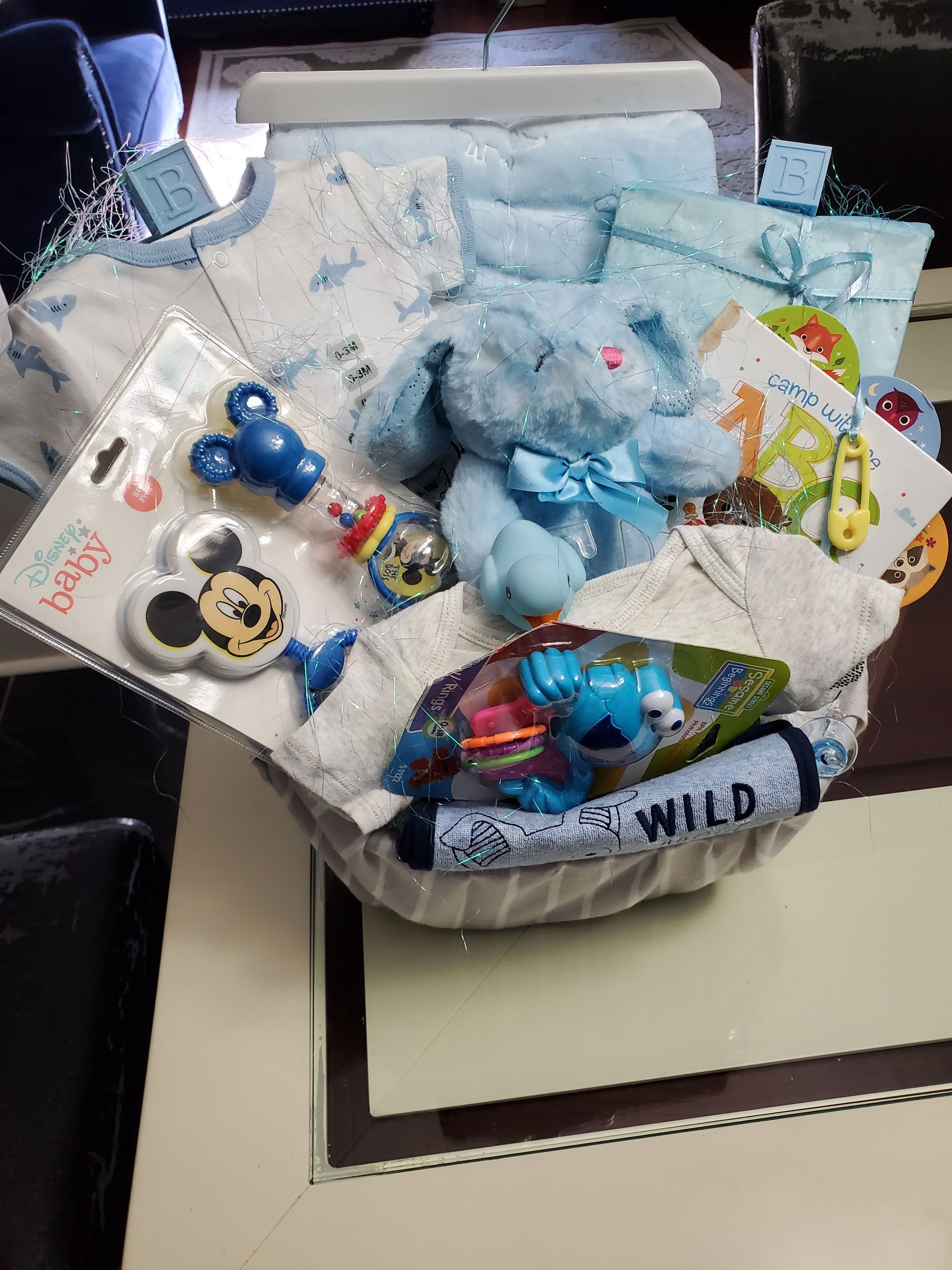 Baby gift basket with blue and white items, including a stuffed bunny, clothes, and toys.