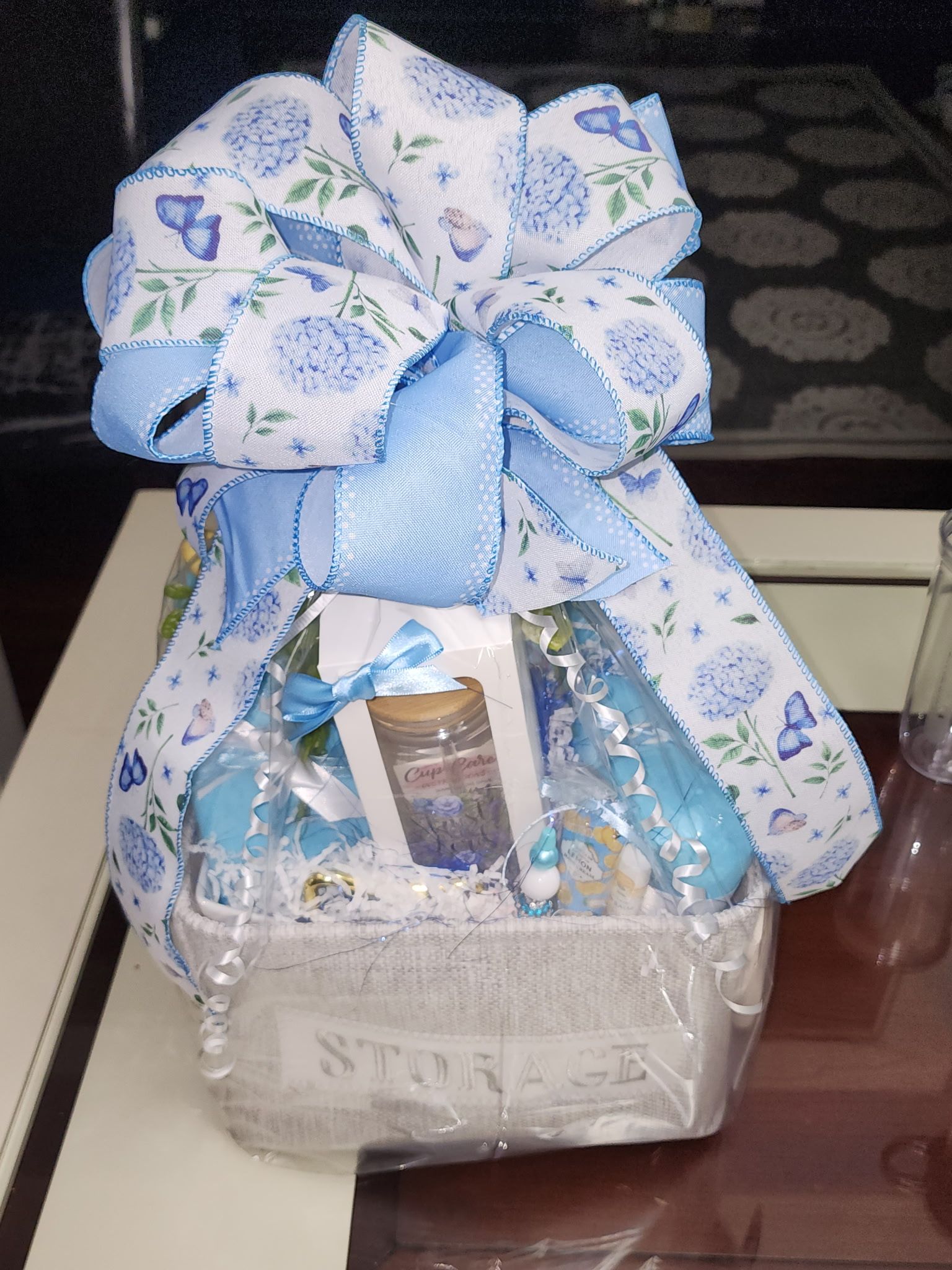 Gift basket with blue and white ribbon, flowers, and assorted items.