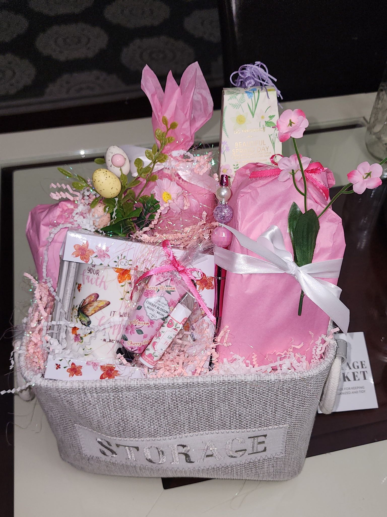 Easter basket with pink gifts, decorations, and flowers on a table.