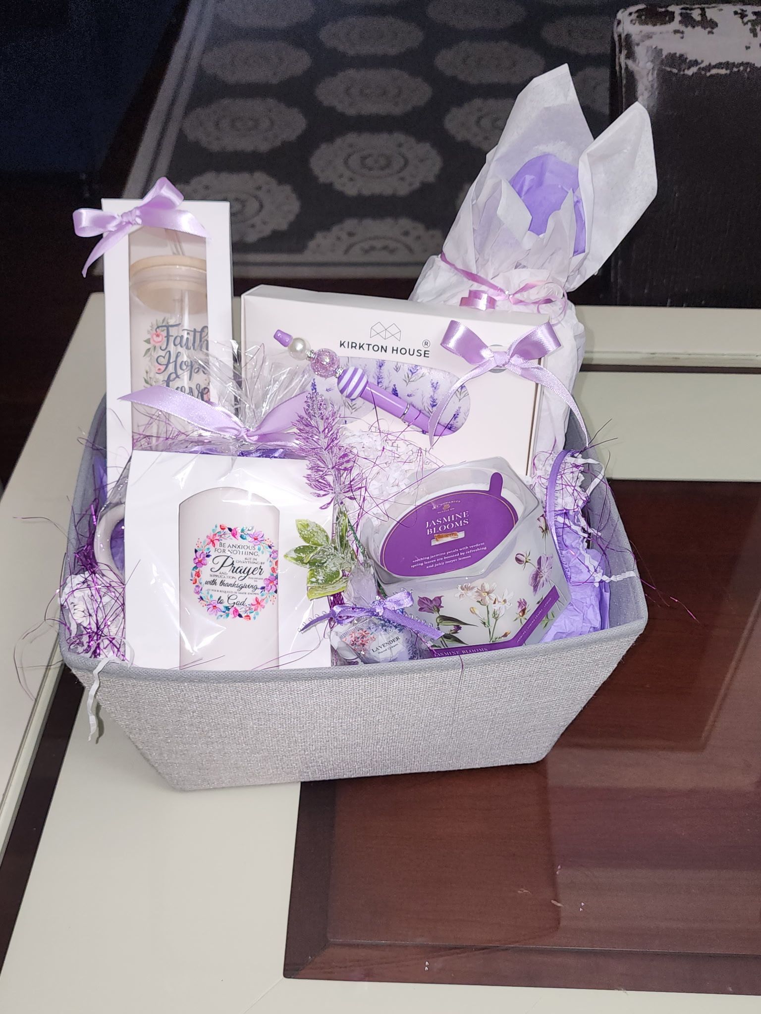 Lavender-themed gift basket with a mug, candle, and ribbon, on a table.