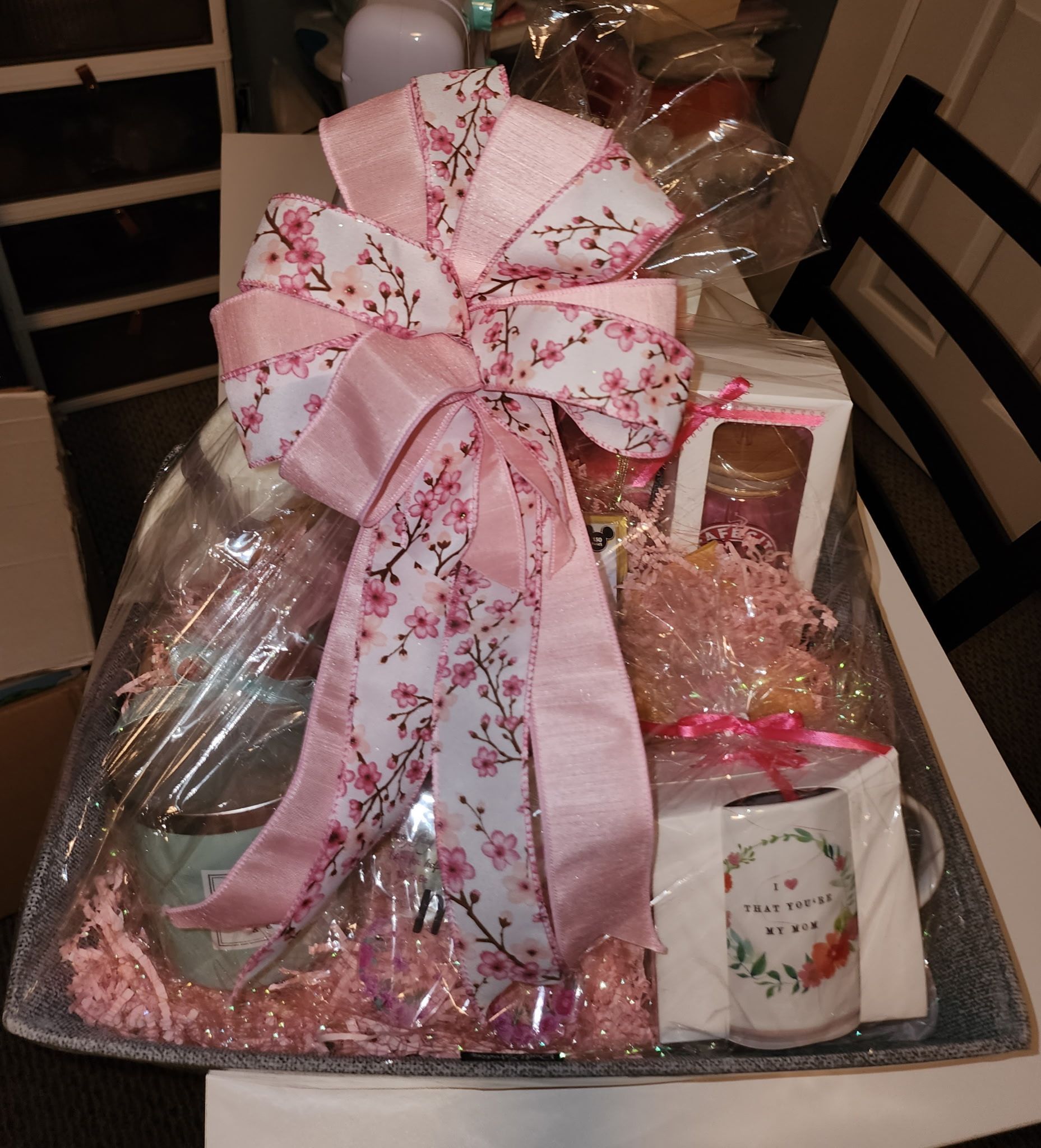Gift basket with pink floral bow and contents: candle, mug, and treats.