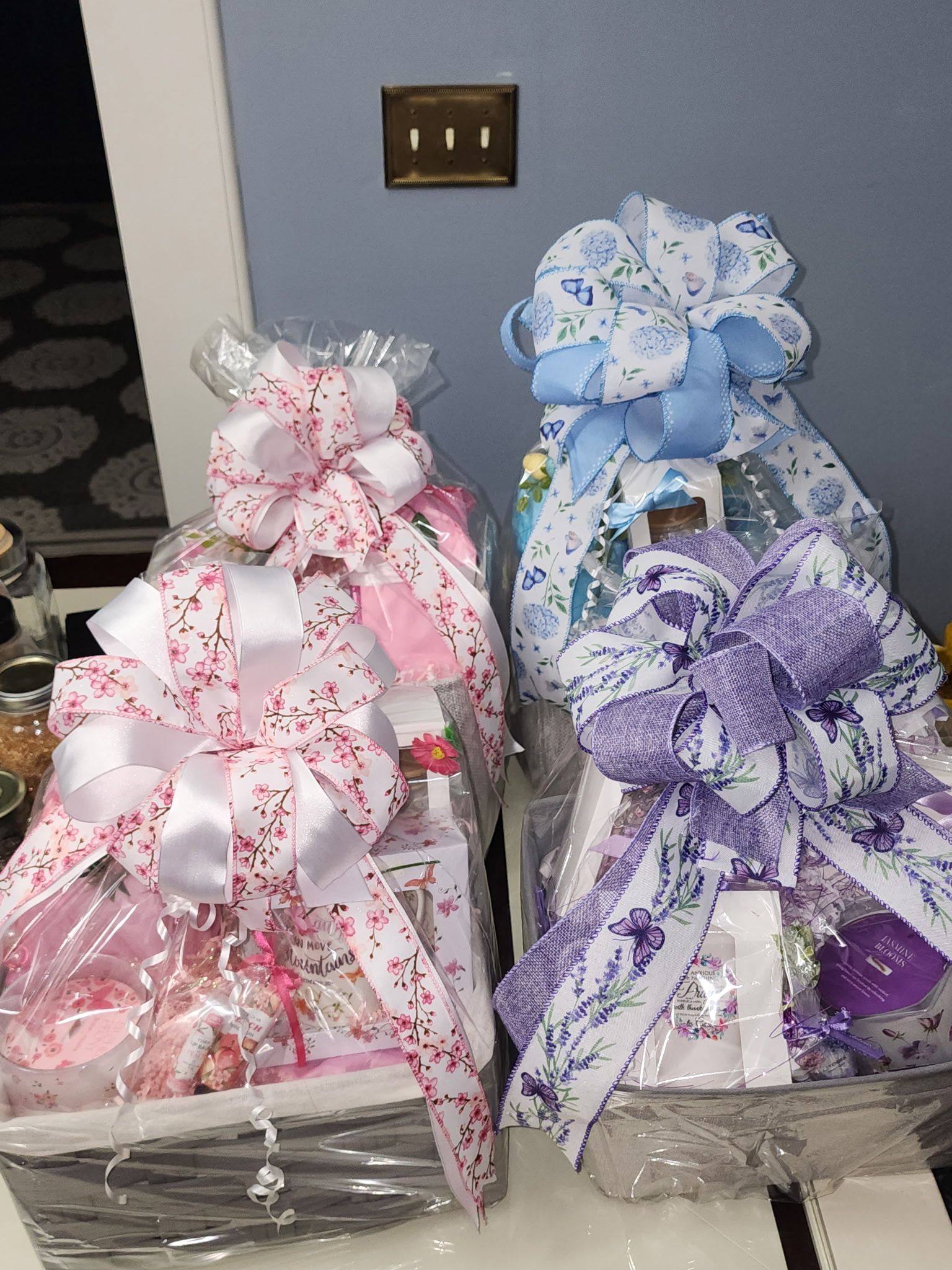 Gift baskets wrapped in cellophane, adorned with floral bows in pink, blue, and purple.