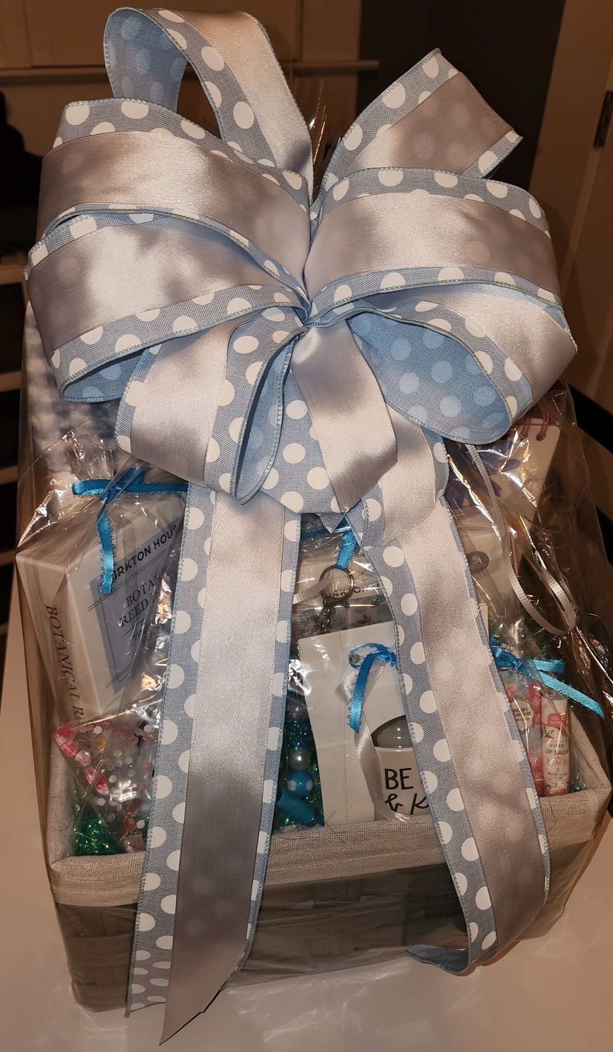 Gift basket with blue and silver ribbon, various items inside.