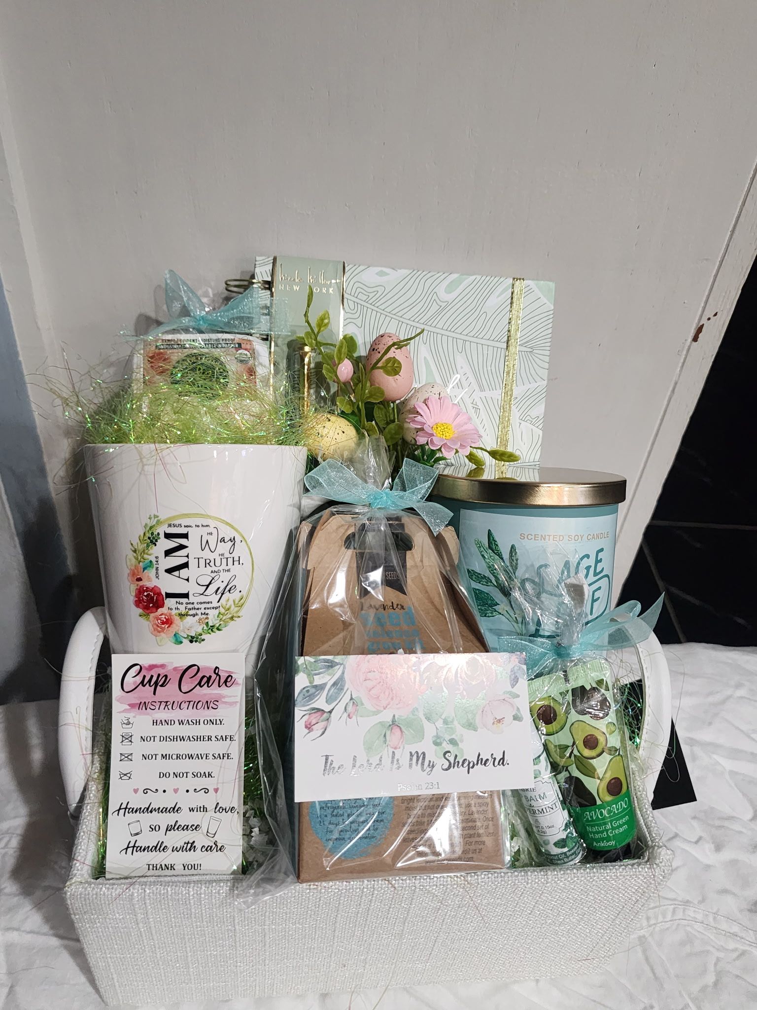 Gift basket with mug, flowers, candle, and treats, in pastel tones.