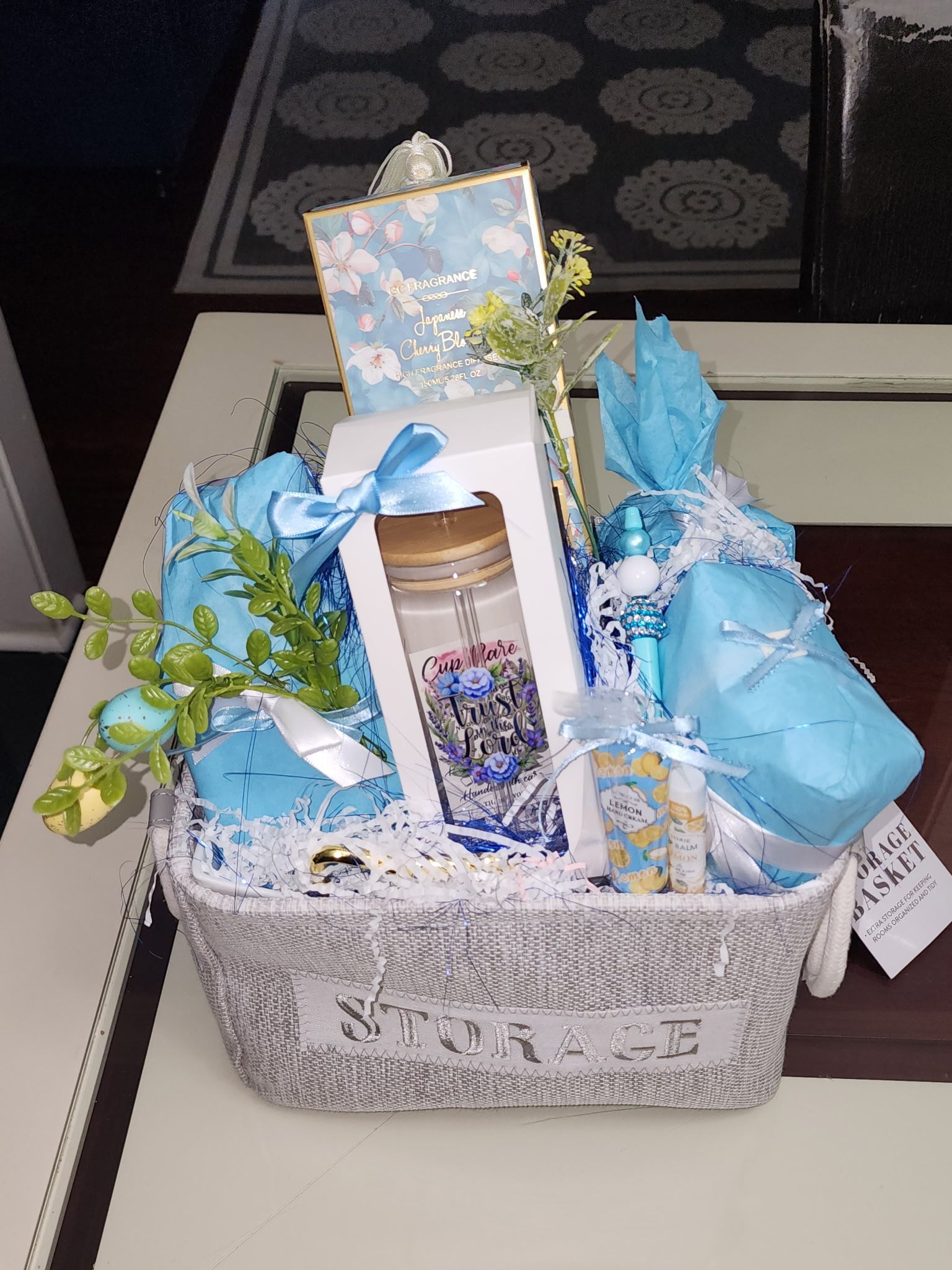 Gift basket with blue and white items on a table, including a card and jar.