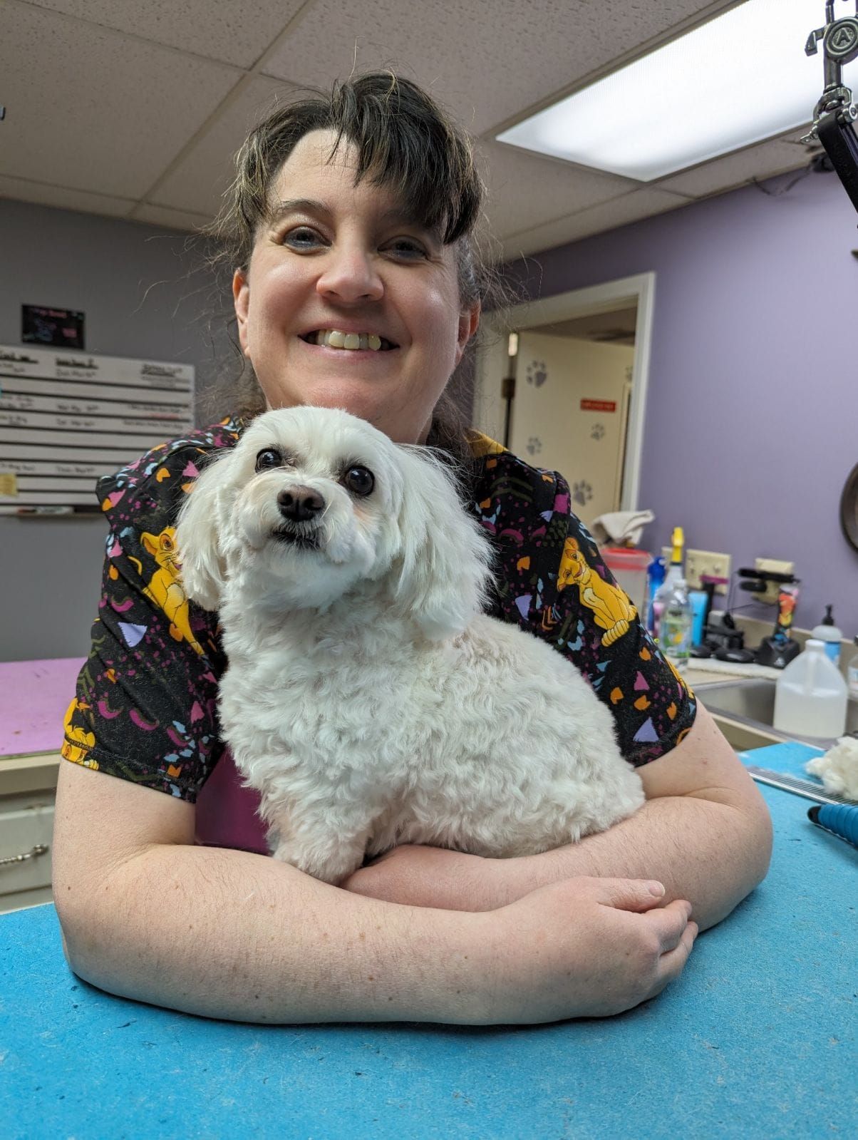 A woman is sitting at a table holding a small white dog.