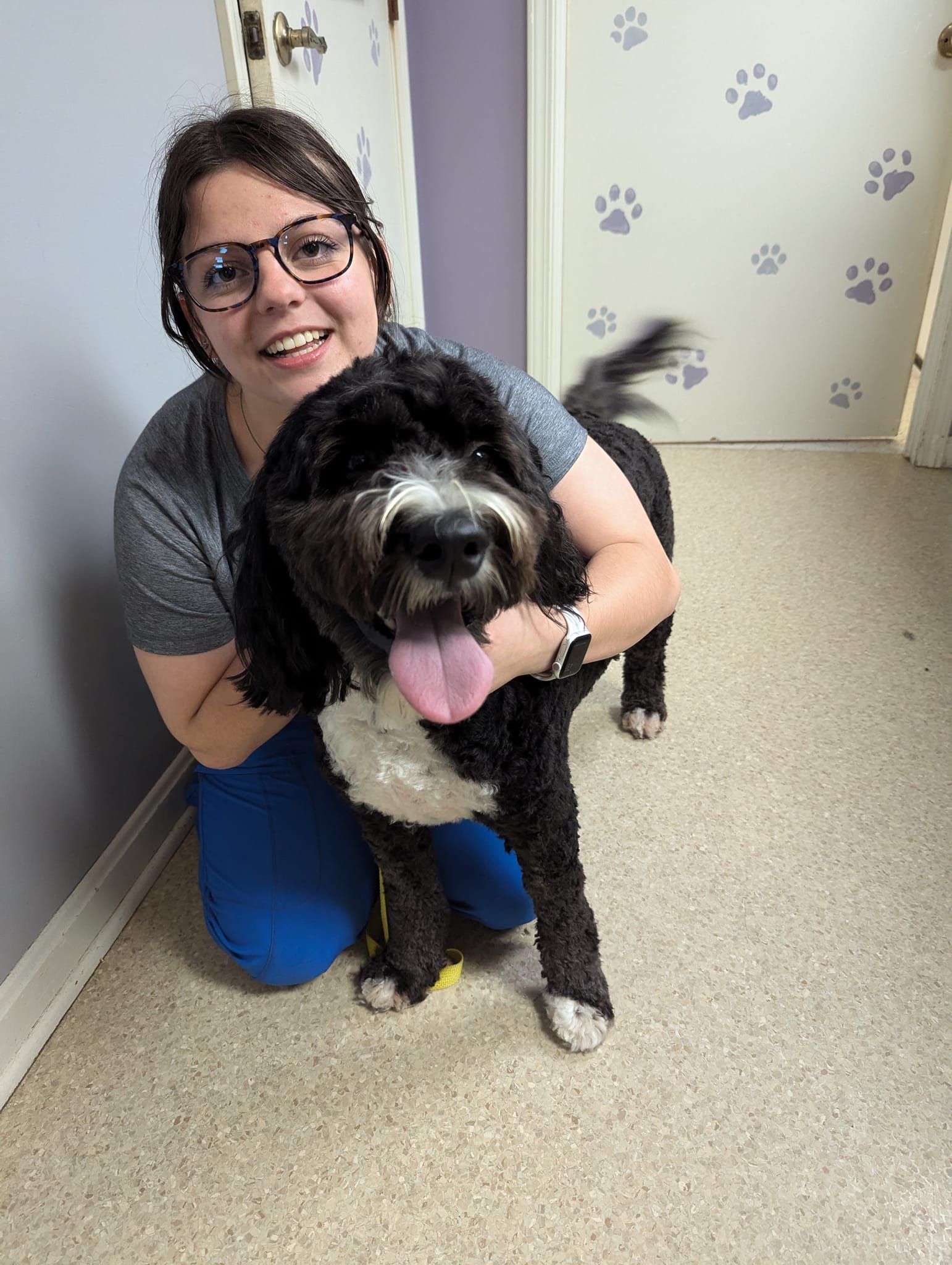 A woman is kneeling down next to a dog with its tongue hanging out.