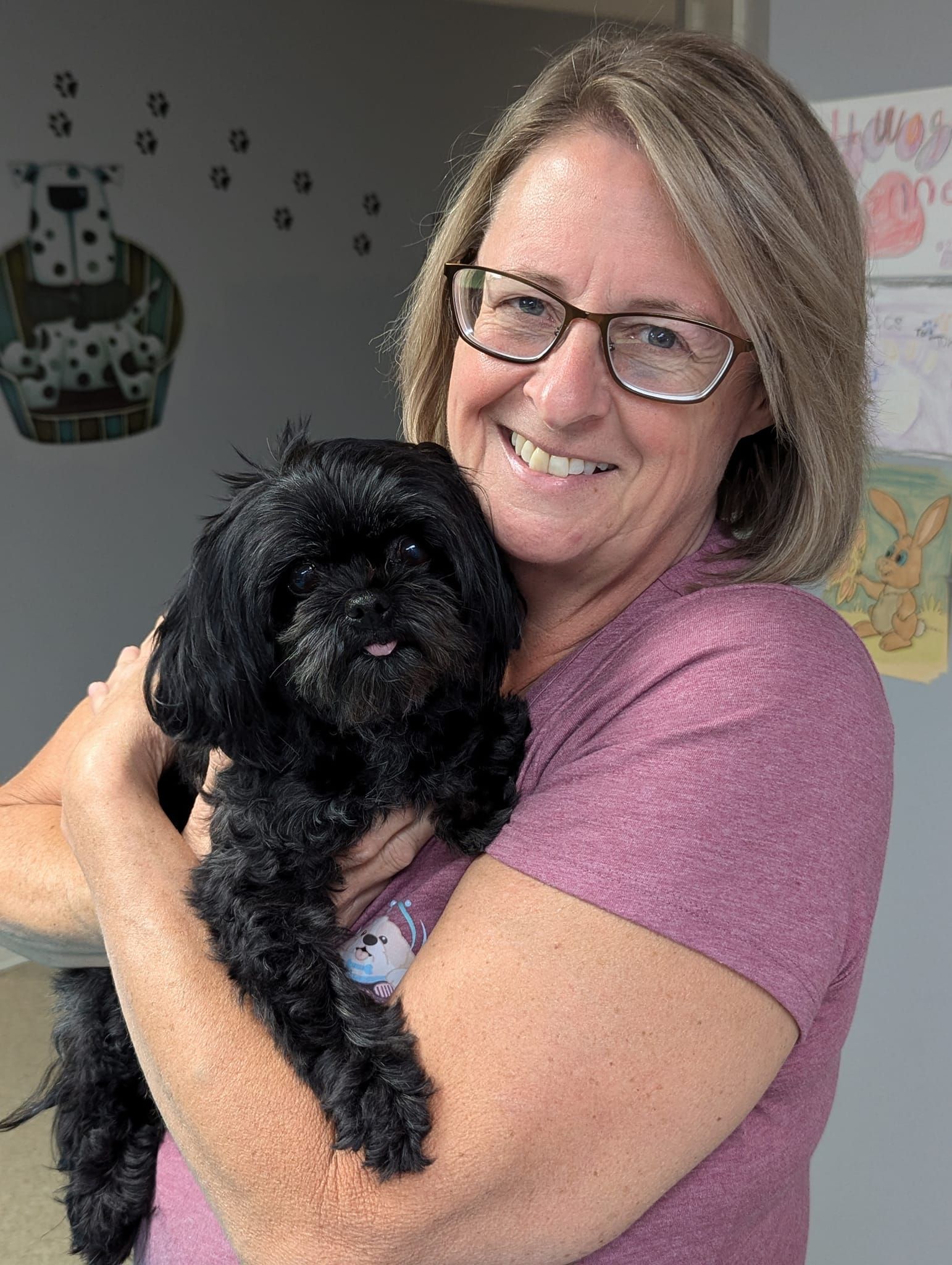 A woman is holding a small black dog in her arms.