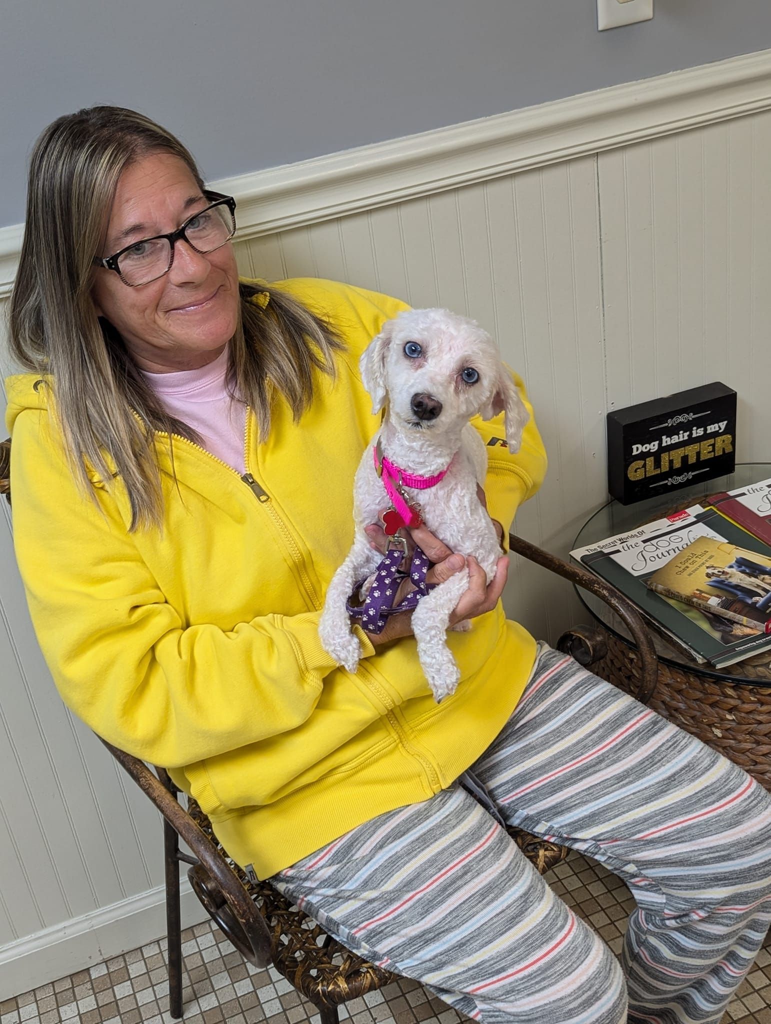 A woman is sitting in a chair holding a small white dog.