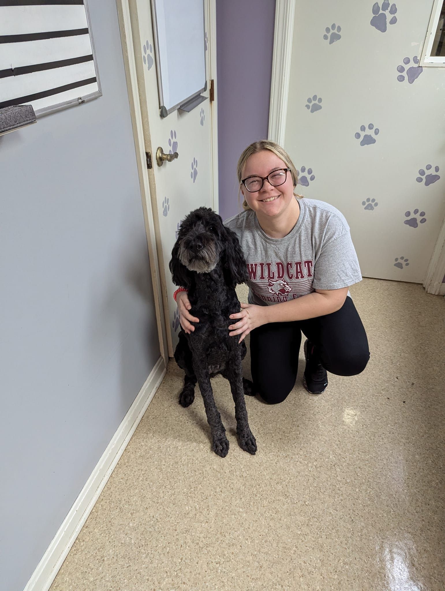 A woman is kneeling down next to a dog in a hallway.