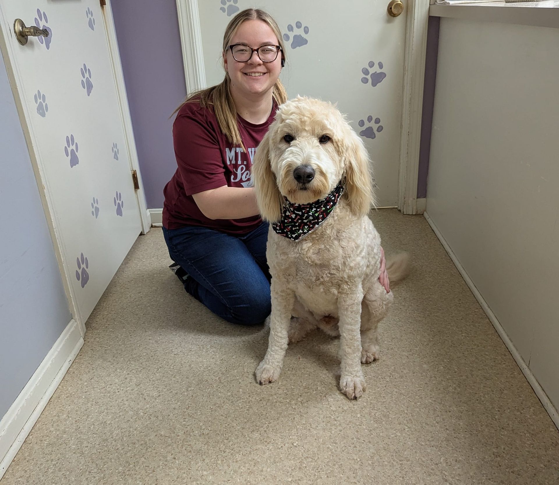 A woman is kneeling down next to a dog in a hallway.
