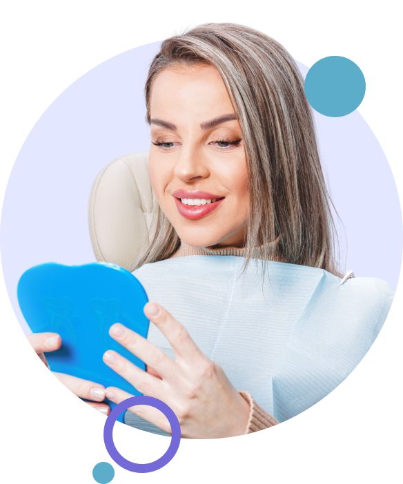 Woman sitting in a dental chair looking at herself in a handheld mirror