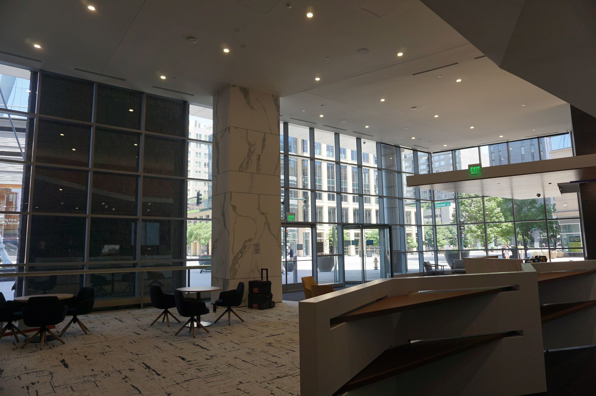 A large lobby with tables and chairs and a green exit sign