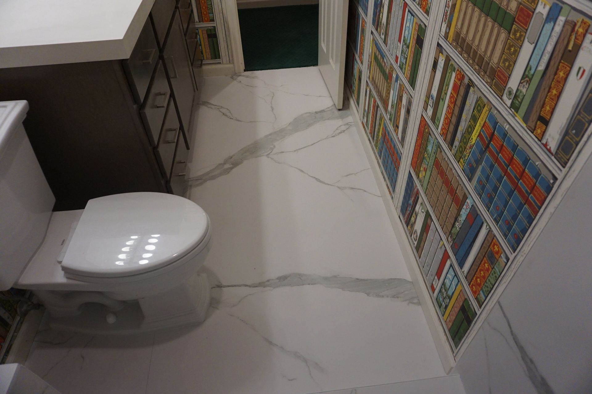 A toilet is sitting in a bathroom next to a bookshelf.