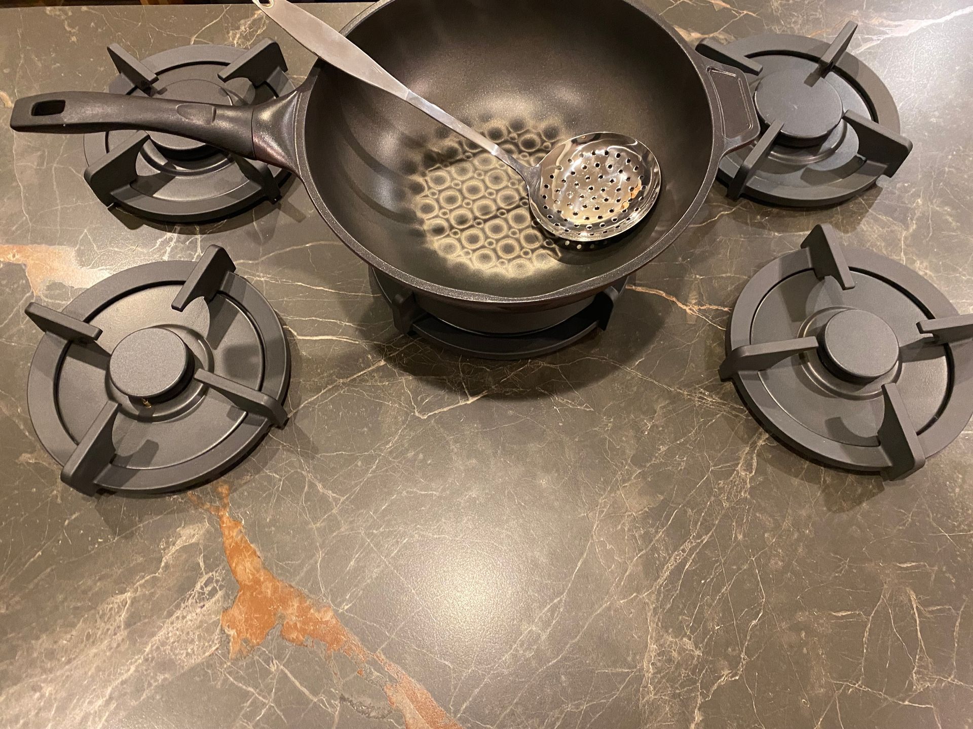 A wok with a ladle in it is cooking on a stove top.