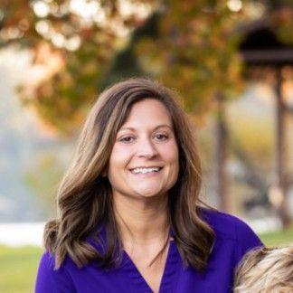 A woman in a purple shirt is smiling while holding a child.