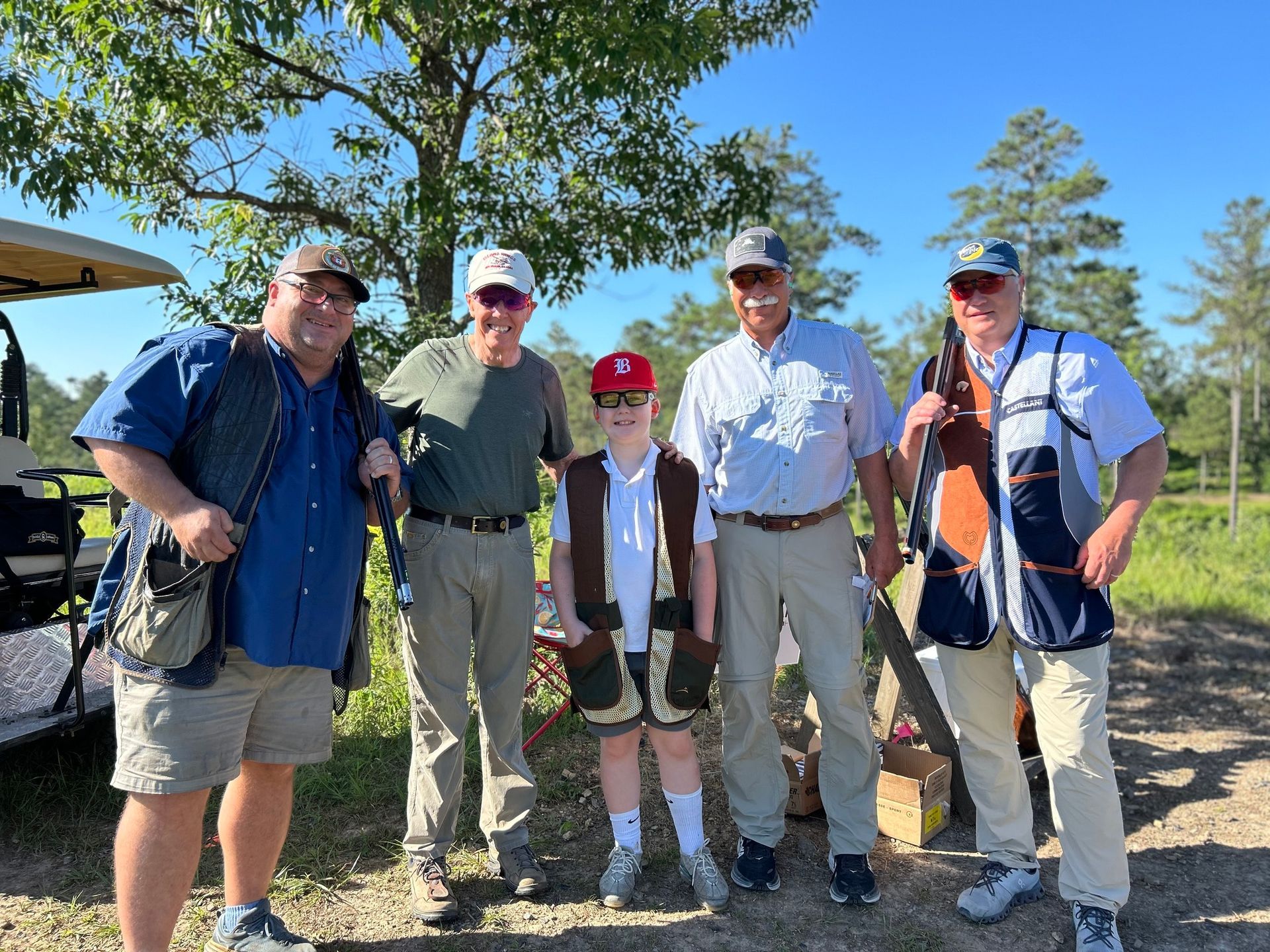 A group of men are standing next to each other in a field holding shotguns. At the targets for TBI clayshoot.