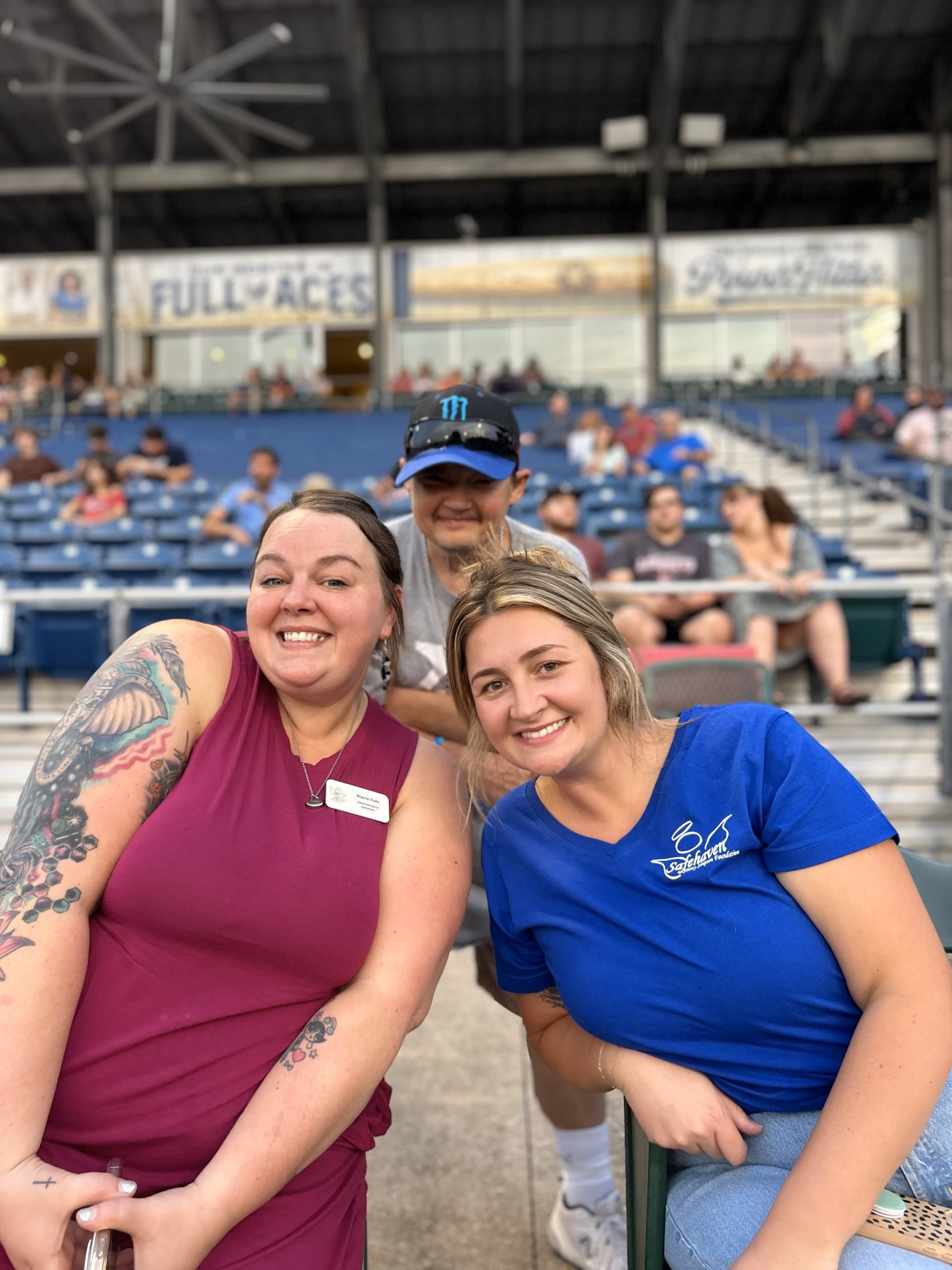 Three people are posing for a picture in a baseball stadium during a support group outing.